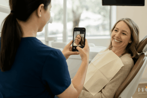 Team member wearing scrubs takes a video of a smiling patient in the dental chair for social media content inside a modern dental office.